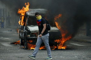 A young man walks past a burning car during a riot in December, 2016. https://flic.kr/p/Poy6uq